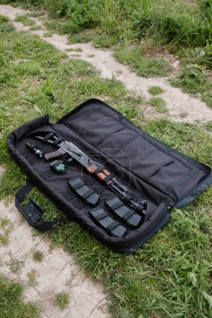 Foto de Funda de pistola descubierta con AK-47, cargadores y linterna tumbados en el suelo negro - Imagen libre de derechos