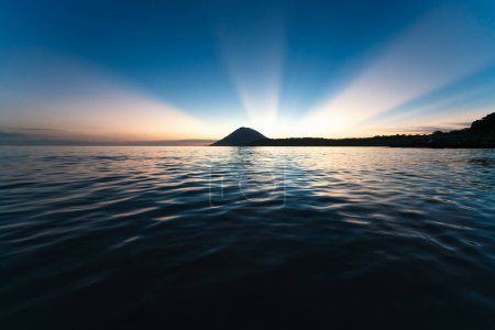 Téléchargez les photos : Coucher de soleil spectaculaire sans nuages avec des rayons de soleil derrière l'île volcanique de Bunaken, Sulawesi, Indonésie - en image libre de droit