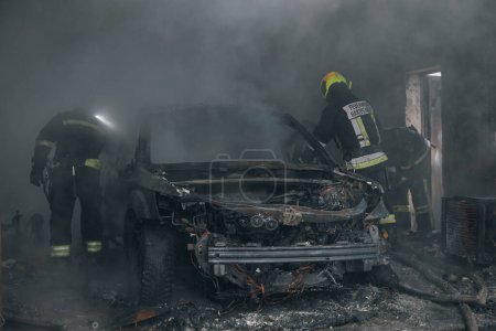 Photo for Firefighters extinguish a burning car in a garage. Burnt car. Rescuers. Strong smoke. Emergency. Insurance case. - Royalty Free Image