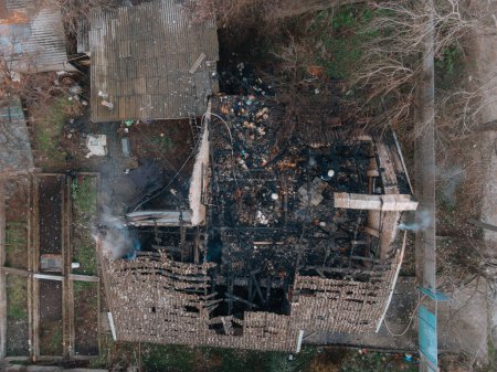 Top view of a burnt house. The house was completely destroyed by fire. The roof collapsed, the walls turned black. Burnt items are scattered around the house. Fire in a private house.