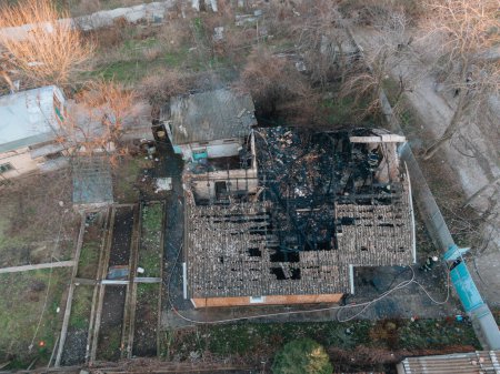 Top view of a burnt house. The house was completely destroyed by fire. The roof collapsed, the walls turned black. Burnt items are scattered around the house. Fire in a private house.