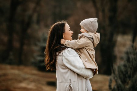 Téléchargez les photos : Mère tenant sa petite fille dans les bras, souriante, à l'extérieur, dans un parc, le jour d'automne. - en image libre de droit