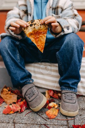 Foto de Closeup of a child holding a slice of pizza, outdoors on city streets. - Imagen libre de derechos