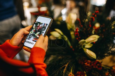 Photo for Woman taking pictures of a floral composition with a smartphone at a workshop. - Royalty Free Image