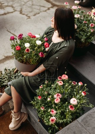 Photo for Woman sitting on stairs at a flower shop holding a big flower pot with ranunculus flowers. - Royalty Free Image