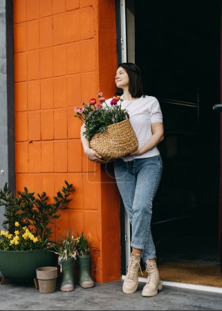Photo for Florist working at a flower shop. Woman a big basket with pink flowers. - Royalty Free Image