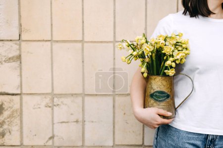 Téléchargez les photos : Gros plan d'une femme tenant un vase avec de petites fleurs de jonquille. - en image libre de droit