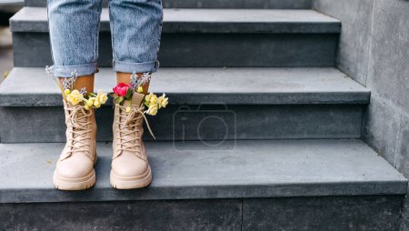 Closeup of female feet in boots with different colorful spring flowers inside.