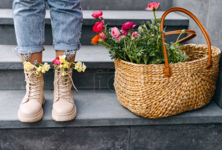 Photo for Female feet in boots with different colorful spring flowers inside next to a big basket with flowers. Flower shop concept. - Royalty Free Image