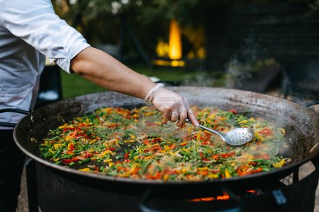 Photo for Chef cooking vegetables in a big pan, outdoors. - Royalty Free Image