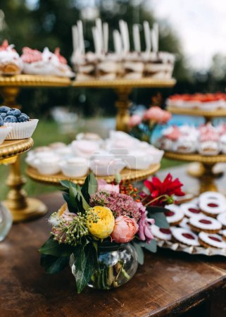 Foto de Un bar de dulces en una fiesta. Ramo de rosas amarillas en una mesa con diferentes postres hechos a mano. - Imagen libre de derechos