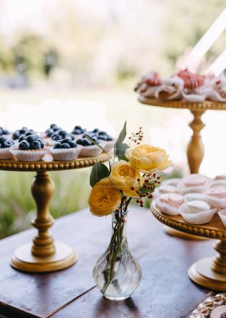 Foto de Un bar de dulces en una fiesta. Ramo de rosas amarillas en una mesa con diferentes postres hechos a mano. - Imagen libre de derechos