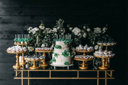 Foto de Un bar de dulces en una boda. Mesa dulce con pastel de boda y diferentes postres hechos a mano en tonos verdes y blancos. - Imagen libre de derechos