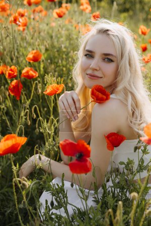 Téléchargez les photos : Portrait d'une jeune femme blonde dans un champ avec des coquelicots rouges sauvages, souriant, regardant la caméra. - en image libre de droit