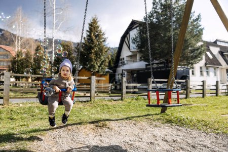 Photo for Child on swing at a playground on spring sunny day, playing with soap bubbles. - Royalty Free Image