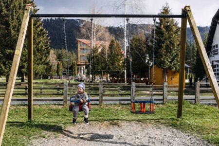 Téléchargez les photos : Enfant en balançoire sur une aire de jeux au printemps journée ensoleillée. - en image libre de droit