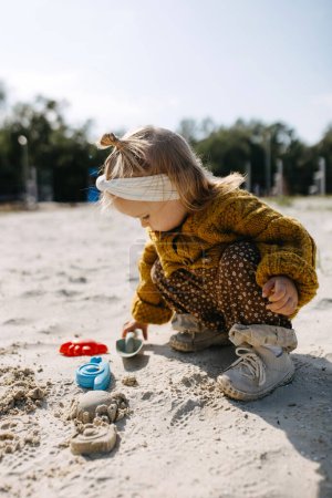 Foto de Una niña jugando en la arena en un parque infantil, con moldes de arena y una pala. - Imagen libre de derechos
