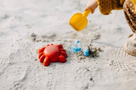 Foto de Primer plano de un niño jugando con moldes de arena y una pala sobre arena blanca. - Imagen libre de derechos