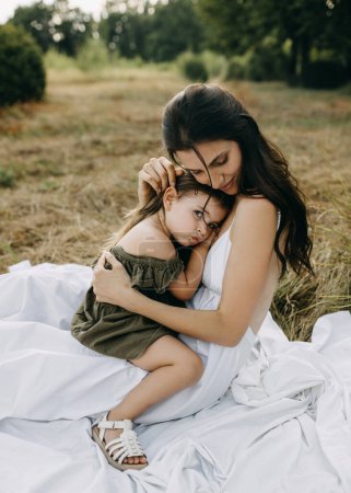 Foto de Madre sosteniendo a su pequeña hija triste en brazos, reconfortando y avivando su cabeza, al aire libre. - Imagen libre de derechos
