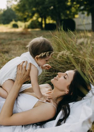 Téléchargez les photos : Mère jouant et parlant à son bébé, couchée sur l'herbe dans un parc, le jour de l'été. - en image libre de droit