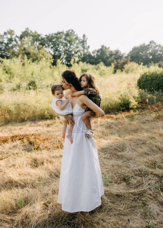 Téléchargez les photos : Mère tenant ses deux filles dans les bras, dehors dans un parc un jour d'été. - en image libre de droit