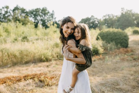 Photo for Happy moment of mother playing with her daughter outdoors in a park on a summer day, laughing. Piggyback riding. - Royalty Free Image
