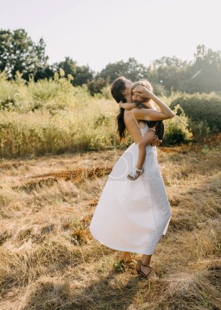 Photo for Mother holding her little daughter in arms, outdoors, walking in a field. - Royalty Free Image