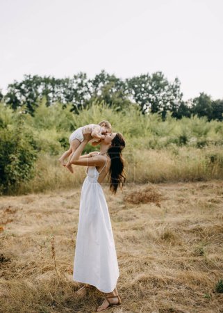 Photo for Mother holding baby up in arms, cuddling and kissing on nose, outdoors in a park on summer day. - Royalty Free Image