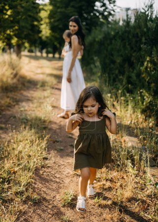 Téléchargez les photos : Petite fille folle s'éloignant de sa mère en marchant dans un parc le jour de l'été. - en image libre de droit