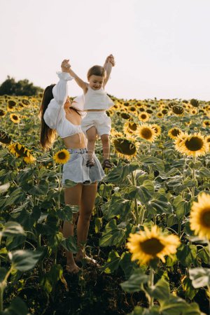 Foto de Madre jugando con su hijita, levantándola, en un interminable campo de girasoles. - Imagen libre de derechos