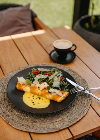 Téléchargez les photos : Omelette au fromage et salade dans une assiette, avec une tasse de café, sur une table en bois à la terrasse du café. - en image libre de droit