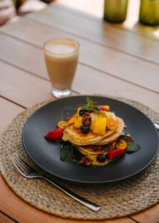 Téléchargez les photos : Crêpes garnies de fruits et de noix, servies avec un latte sur une table en bois. - en image libre de droit