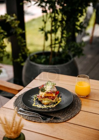 Photo for Waffle sandwich with ham, vegetables and cheese, served with orange juice, placed on a wooden table at a terrace on a summer day. - Royalty Free Image