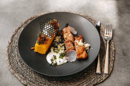 Foto de Polenta y carne con una salsa cremosa en un plato negro, entorno al aire libre en una terraza cafetería. - Imagen libre de derechos