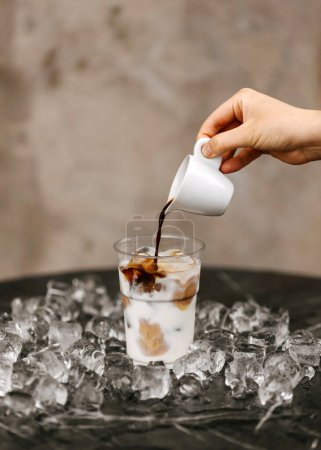 Foto de Verter el espresso en un vaso de leche helada, rodeado de cubitos de hielo. - Imagen libre de derechos