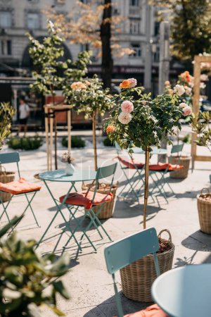 Foto de Tranquilo entorno de café al aire libre con rosas florecientes y muebles de metal azul. - Imagen libre de derechos