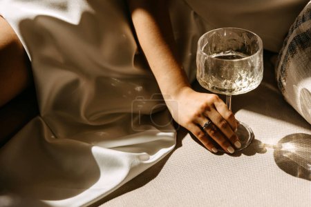 Téléchargez les photos : Main féminine avec bague de fiançailles en diamant tenant une coupe de champagne au soleil. - en image libre de droit