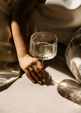 Téléchargez les photos : Une main avec bague de fiançailles en diamant tenant une coupe de champagne au soleil. - en image libre de droit