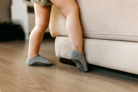 Photo for A toddler's legs in gray anti-slip socks by a beige sofa. - Royalty Free Image