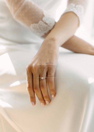Foto de La mano de una mujer con un anillo de compromiso descansa suavemente sobre un vestido de seda blanco - Imagen libre de derechos