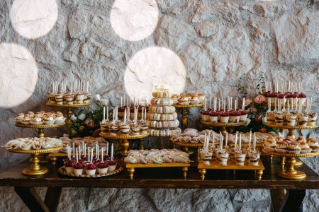 Foto de Una lujosa mesa de postres colocada contra una pared de piedra con soportes dorados. Candy bar en un evento. - Imagen libre de derechos