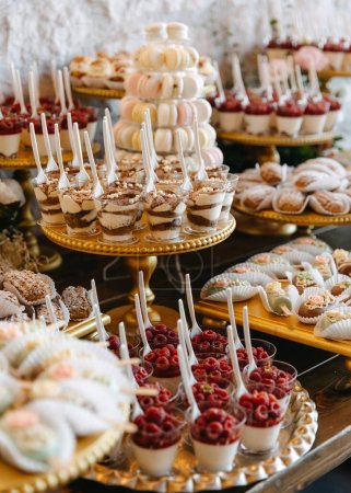 Téléchargez les photos : Une table à dessert lors d'un événement avec une variété de bonbons sur des stands dorés. Barre à bonbons à un mariage. - en image libre de droit