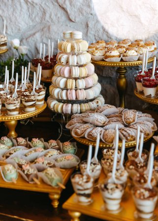 Téléchargez les photos : Une table à dessert lors d'un événement avec une variété de bonbons sur des stands dorés. Barre à bonbons à un mariage. - en image libre de droit
