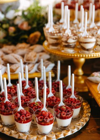 Photo for A dessert table at an event with a variety of sweets on golden stands. Raspberry dessert in cups at a candy bar at a wedding. - Royalty Free Image