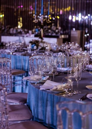 Téléchargez les photos : Une table de réception de mariage élégamment sertie dans des tons bleus avec des assiettes, des verres et des mouchoirs textiles. - en image libre de droit