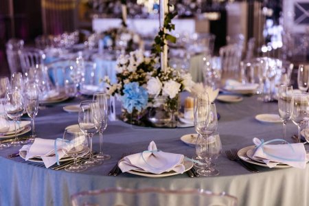 Foto de Una mesa de recepción de boda elegantemente establecida en tonos azules con platos, gafas y pañuelos textiles. - Imagen libre de derechos