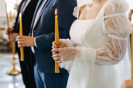 Foto de Una novia y un novio sosteniendo velas amarillas durante una ceremonia de boda en una iglesia. - Imagen libre de derechos