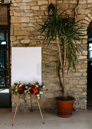 Easel with a white blank welcome board a floral arrangement at a wedding.