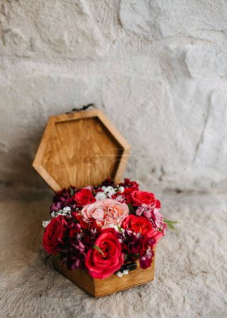 Photo for Wooden hexagon ring box with wedding rings and red and pink roses, on stone textured background. - Royalty Free Image