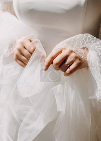 Photo for A bride holding her veil, wearing a diamond engagement ring, in sunlight, closeup. - Royalty Free Image